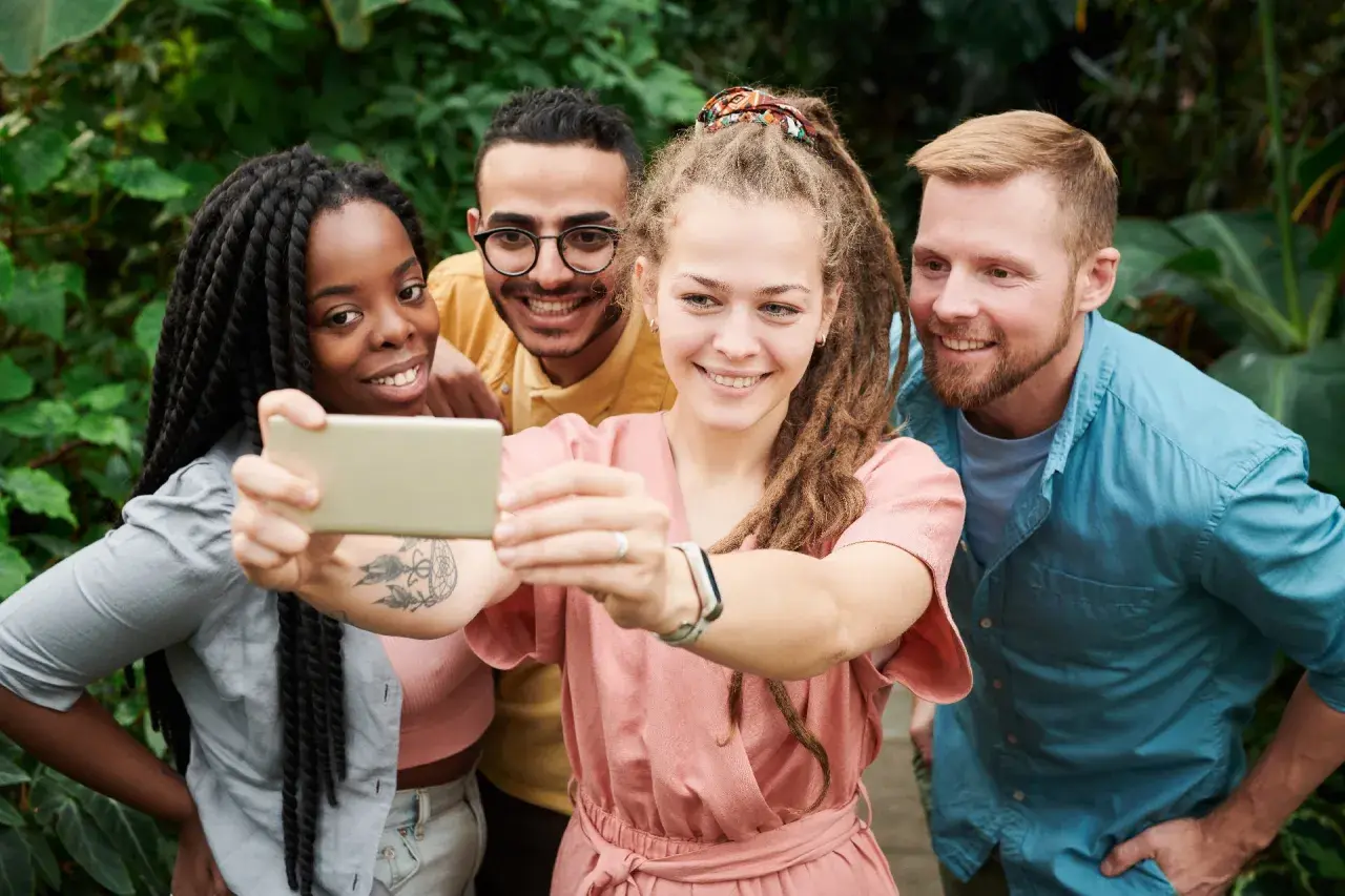 Uśmiechnięci przyjaciele robią selfie w otoczeniu zieleni. Pokazują, że cechy dobrego przyjaciela to wspólne chwile i radość.