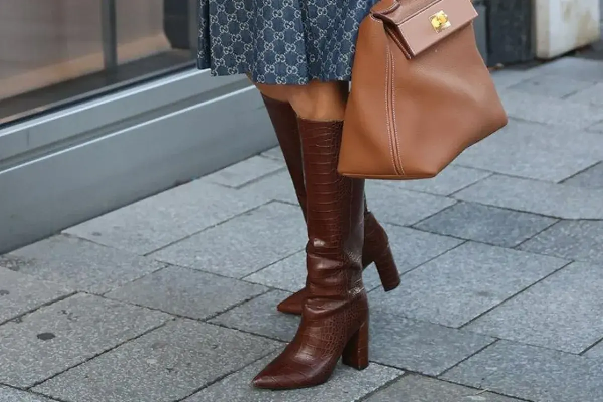 Eleganckie kozaki za kolano w brązowym kolorze, z fakturą skóry krokodyla, idealne na imprezę. Stylizacja uzupełniona o torebkę w tym samym odcieniu.