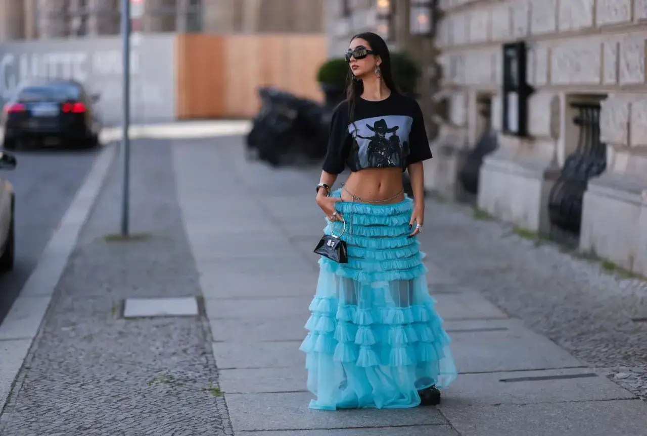 Spódnica tiulowa stylizacje na sportowo: dziewczyna w krótkim T-shircie i błękitnej, falbaniastej spódnicy z tiulu, z małą torebką.