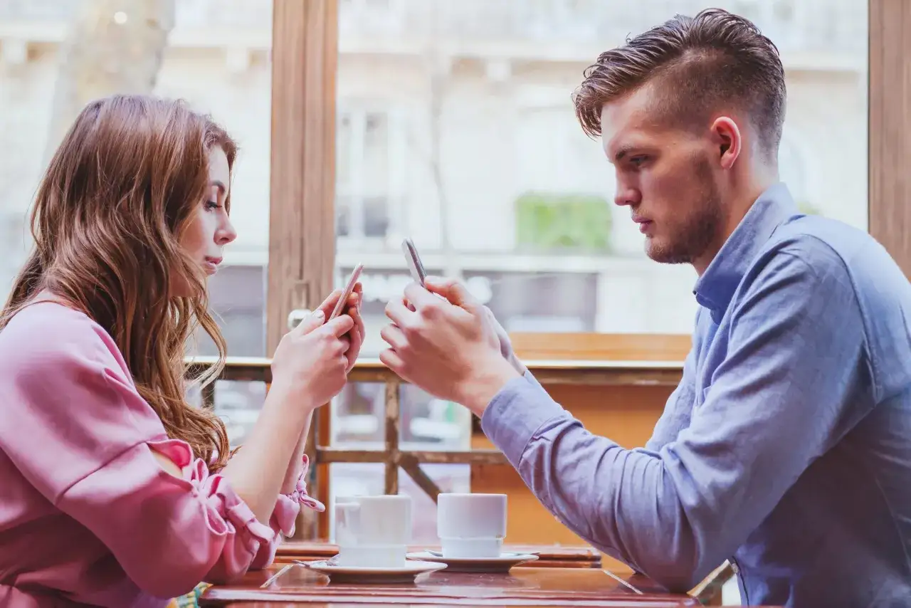 Para siedzi przy stoliku, każde wpatrzone w swój telefon. Brak tematów do rozmów w związku?