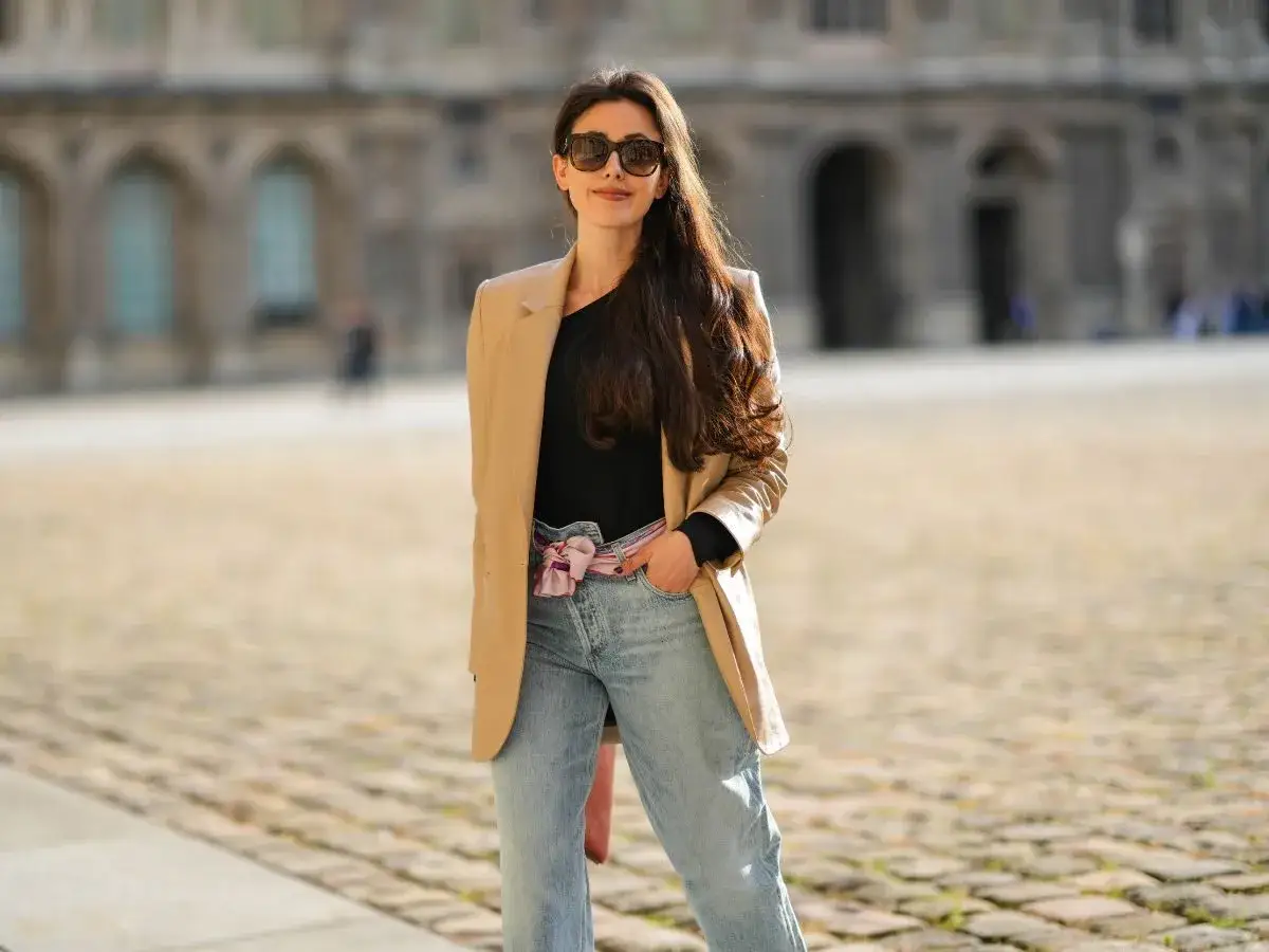 Kobieta w beżowej marynarce i jasnych mom jeans. Idealne buty do mom jeans? Tutaj świetnie sprawdzą się sneakersy lub botki.
