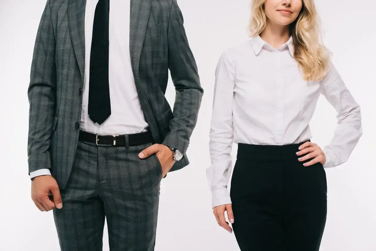 Elegancki mężczyzna w garniturze i kobieta w białej koszuli i czarnych spodniach prezentują r&oacute;żne rodzaje dress code.