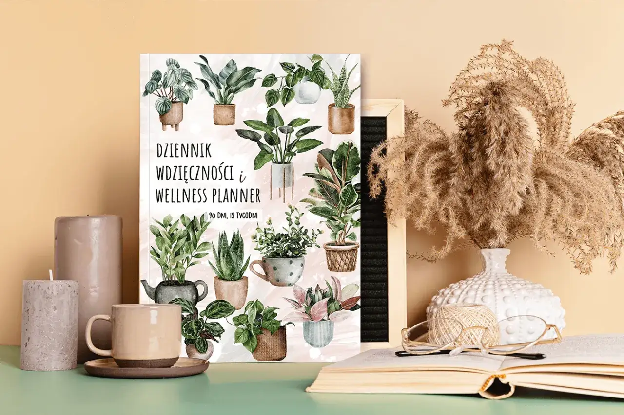 Dziennik wdzięczności i wellness planner z motywem roślinnym. Obok świece, kubek i otwarty notatnik.